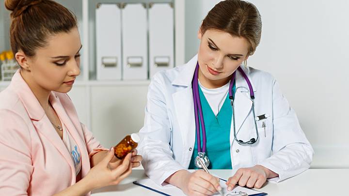 Doctor explaining to woman holding antibiotics why there's a danger in over-prescribing them