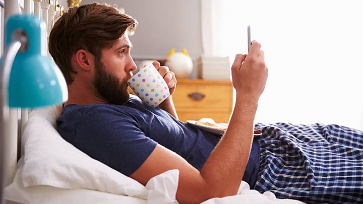 Man looking up painful urination on his phone in bed