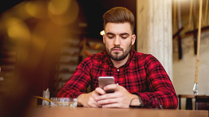 Man in a cafe researching the side effects of Aciclovir on his smart phone
