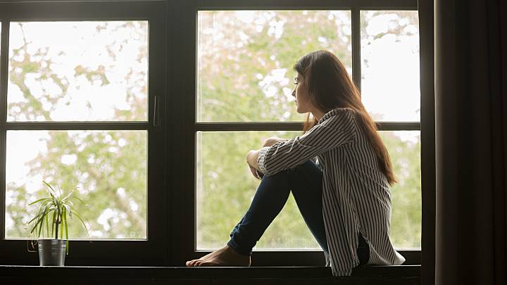 Eine junge Frau sitzt nachdenklich am Fenster. Sie ist ungewollt schwanger und denkt über einen Schwangerschaftsabbruch mit dem Medikament Mifegyne nach.