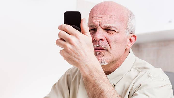 Ein älterer Mann sucht in seinem Smartphone nach Informationen über die Beschwerden seiner Penisverkrümmung.