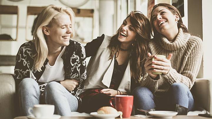 Drei junge, fröhliche Frauen sitzen zusammen in einem Café und unterhalten sich über ihre Gesundheit.