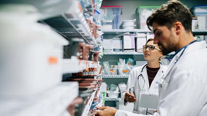 Zwei Apotheker sind im Lager der Apotheke und suchen das passende Potnezmittel für einen Patienten, der dieses dort kaufen wird.