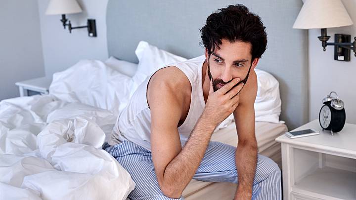 Ein Mann sitzt nachdenklich auf dem Bett. Er hat die Vermutung, dass er an Chlamydien erkrankt ist und muss sich unbedingt testen lassen.