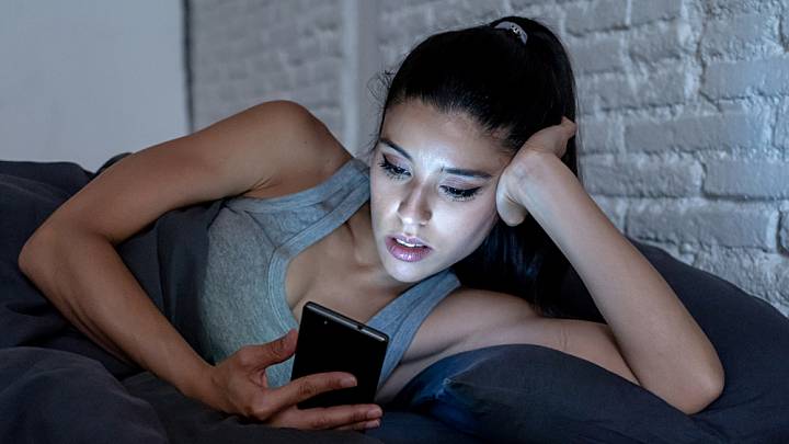 Woman in bed looking up on her phone whether she has thrush or bacterial vaginosis