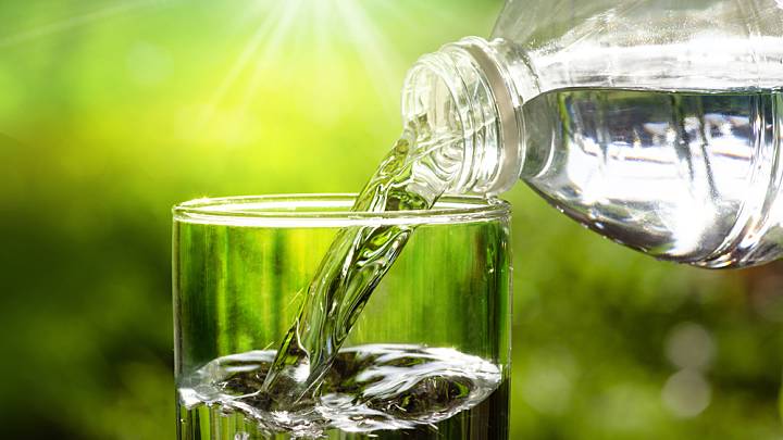 Wasser wird eingeschenkt in Glas aus Flasche, grüner Hintergrund