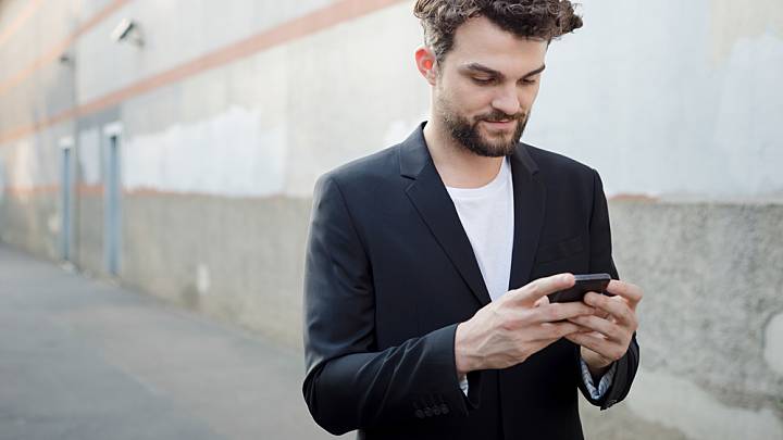 Man looking on his phone for erection pills as he walks down a concrete street
