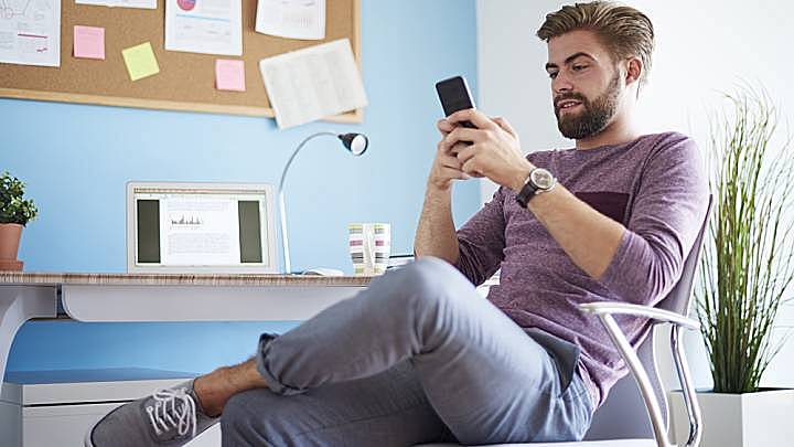 Man sat at his desk at home looking on his phone tips on combating infertility