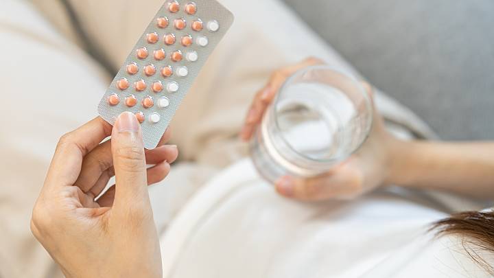Eine Frau hält eine Pillenpackung in der linken Hand und ein Glas Wasser in der anderen