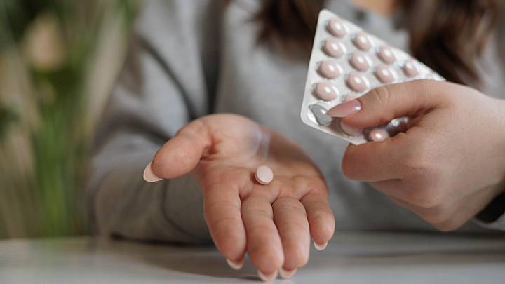 Eine Frau Hat eine Blisterpackung mit Pillten mit dem Wirkstoff Norethisteron in der einen Hand. In der anderen Hand hält Sie eine Tablette die sie aus der Blisterpackung rausgenommen hat.