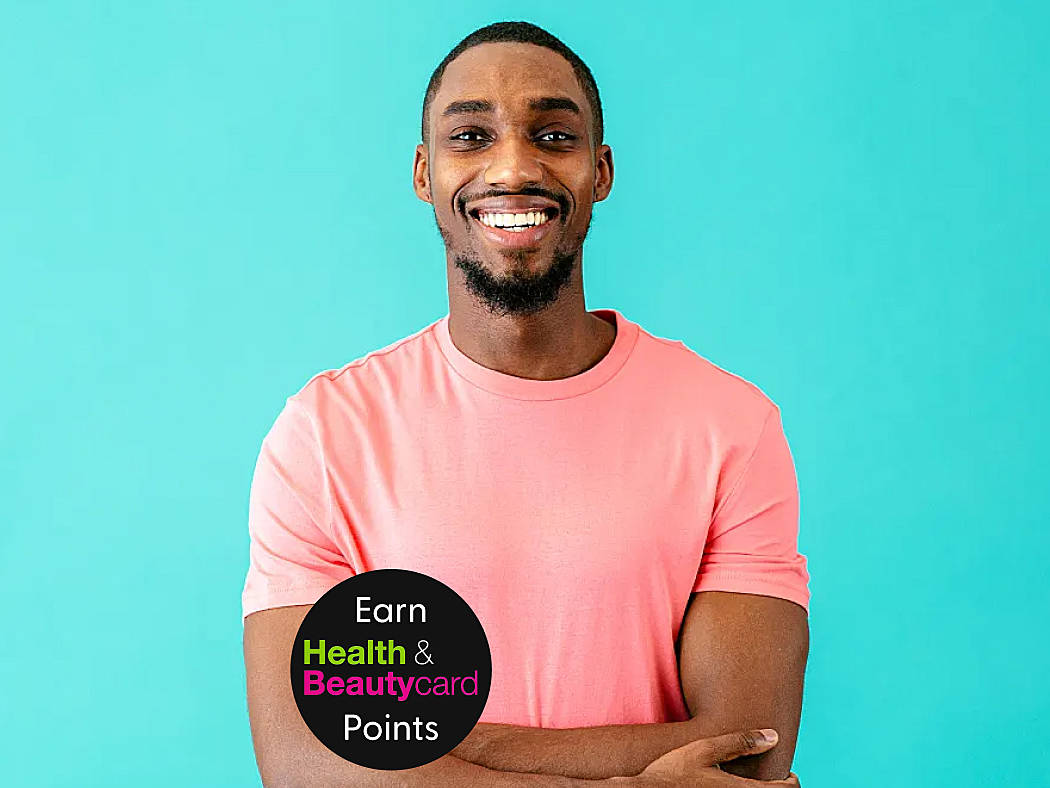 A man wearing a pink t shirt is smiling because he is happy with his testosterone replacement therapy