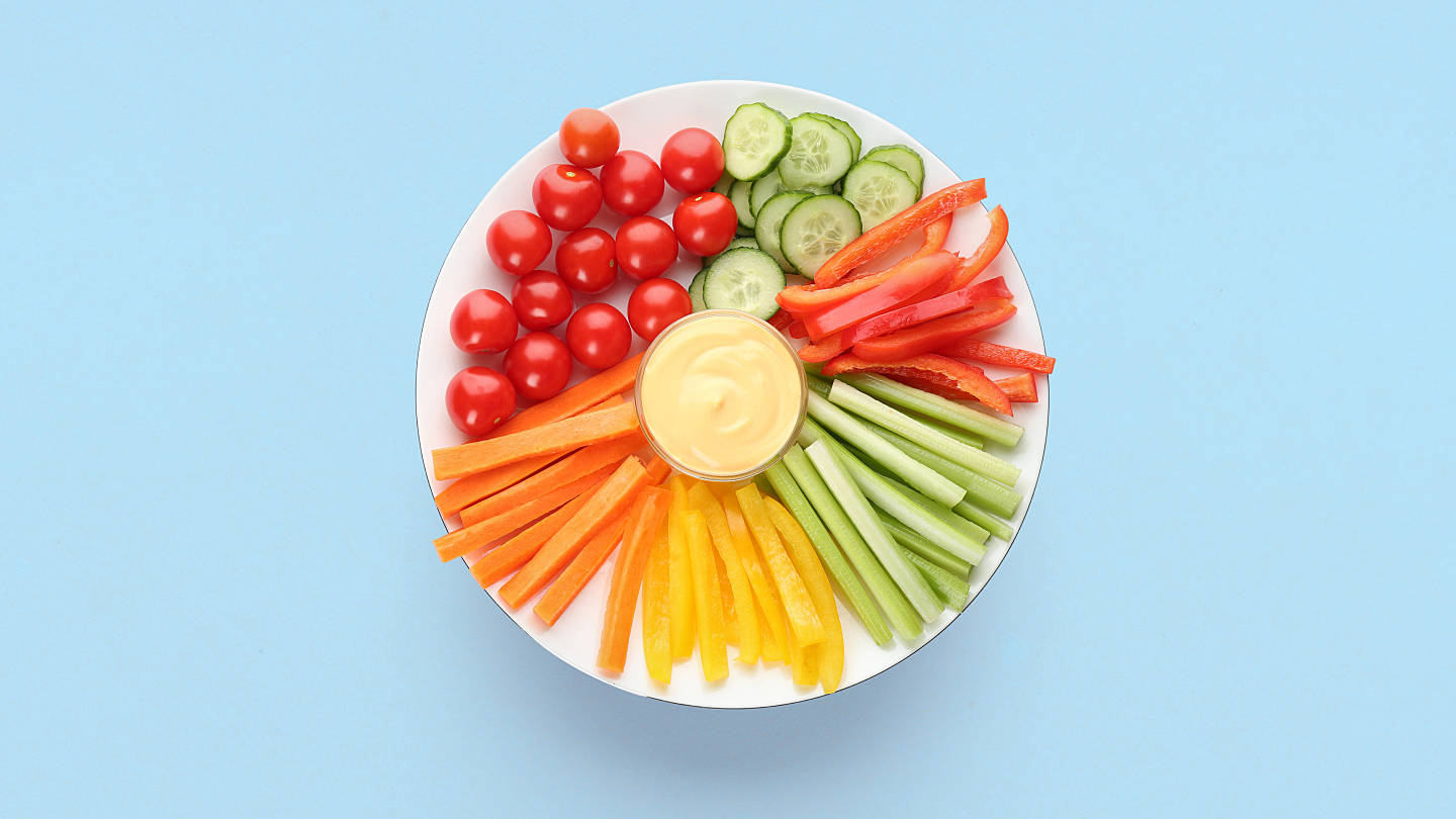 Ein Teller mit einer Auswahl an Gemüse (Tomaten, Gurken, Paprika, Karotten, Sellerie) und ein Dip in der Mitte