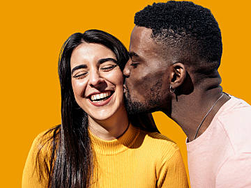 black man in pink t shirt kissing asian woman who is smiling