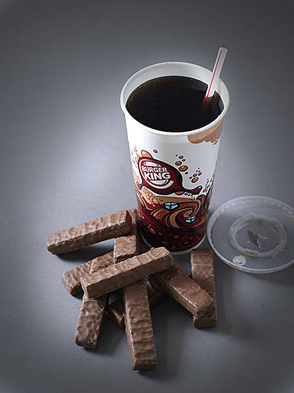 cup of burger king super size coke next to a pile of chocolate wafer bars.