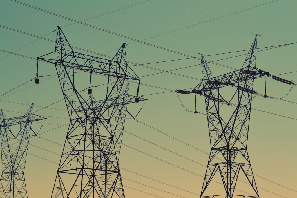 High-voltage lattice transmission towers carrying multiple circuits against a dusk sky.