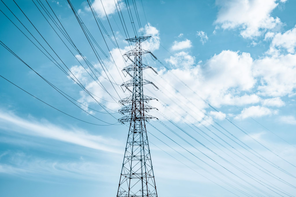 A tall lattice transmission tower carrying multiple circuits against a bright sky.