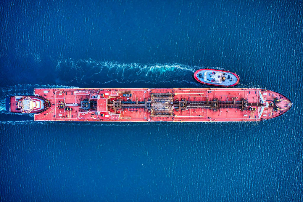 An aerial view of a red oil tanker at anchor in harbour waters.