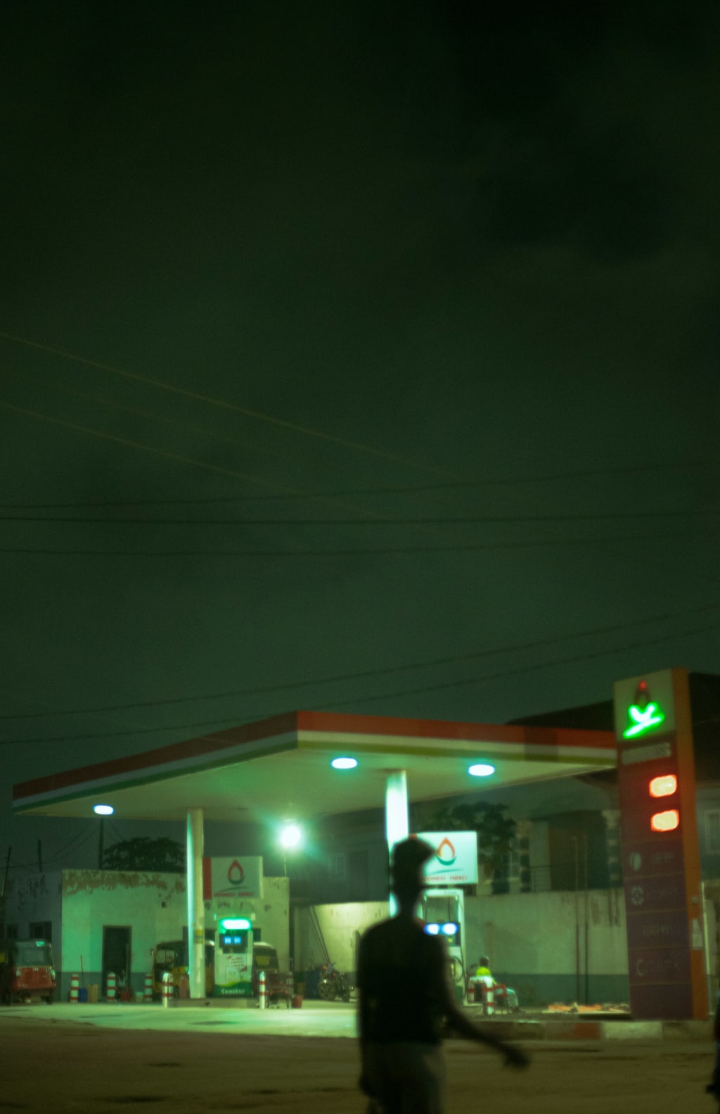 A filling station at night, with people walking through the forecourt.