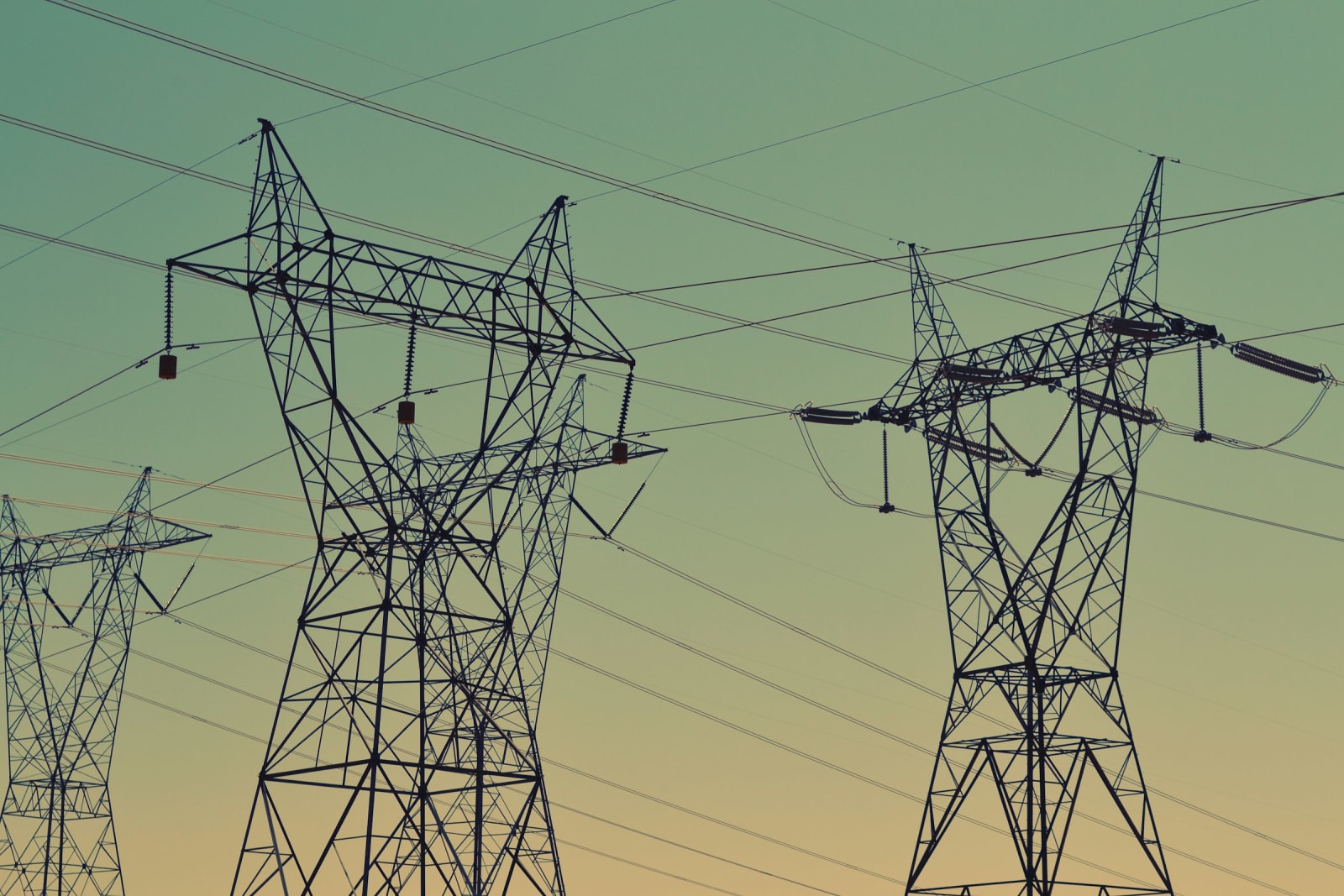 High-voltage lattice transmission towers carrying multiple circuits against a dusk sky.