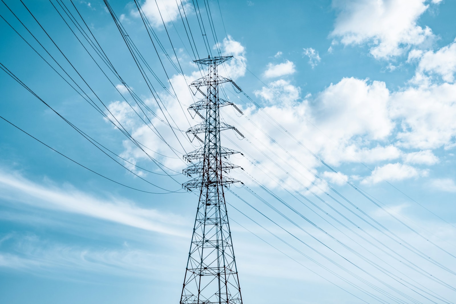 A tall lattice transmission tower carrying multiple circuits against a bright sky.