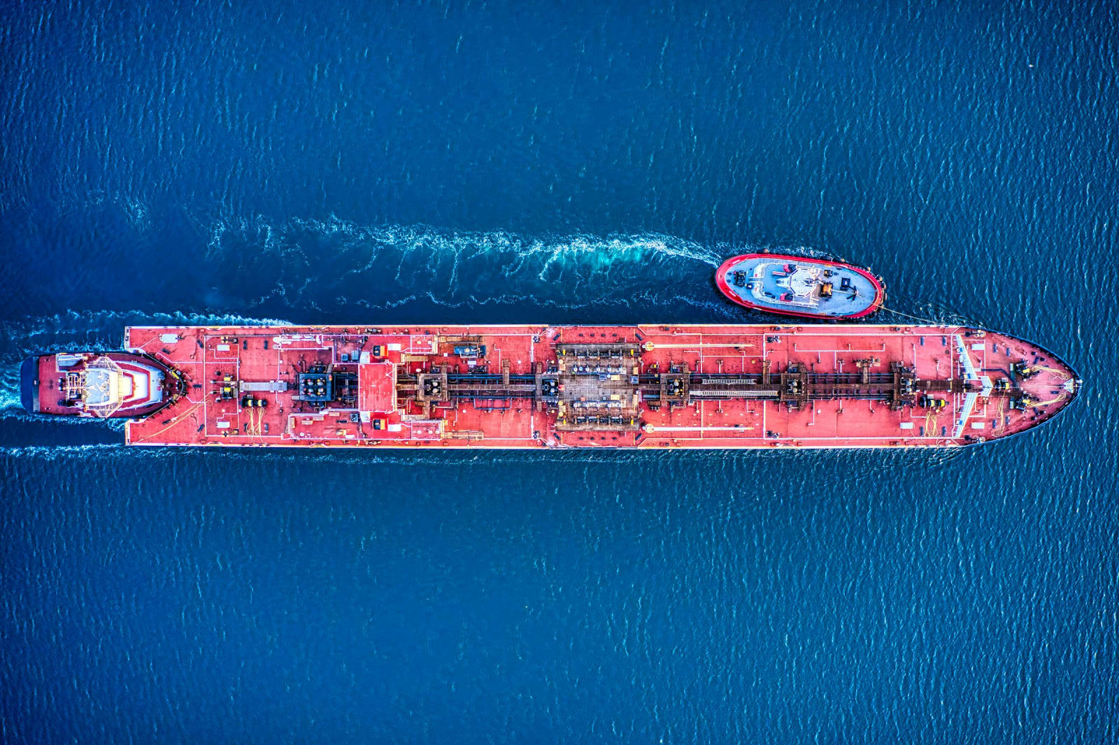 An aerial view of a red oil tanker at anchor in harbour waters.
