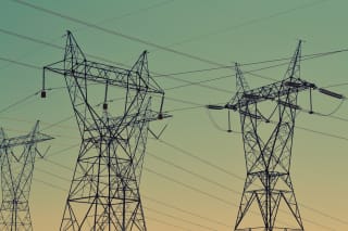 High-voltage lattice transmission towers carrying multiple circuits against a dusk sky.