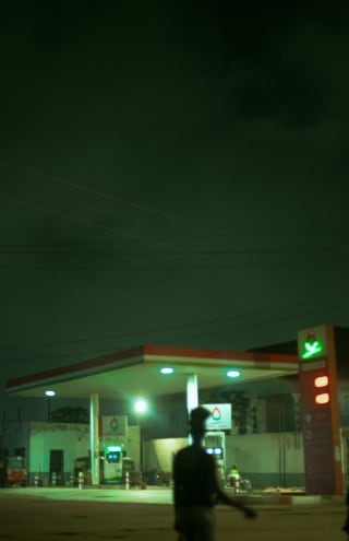 A filling station at night, with people walking through the forecourt.