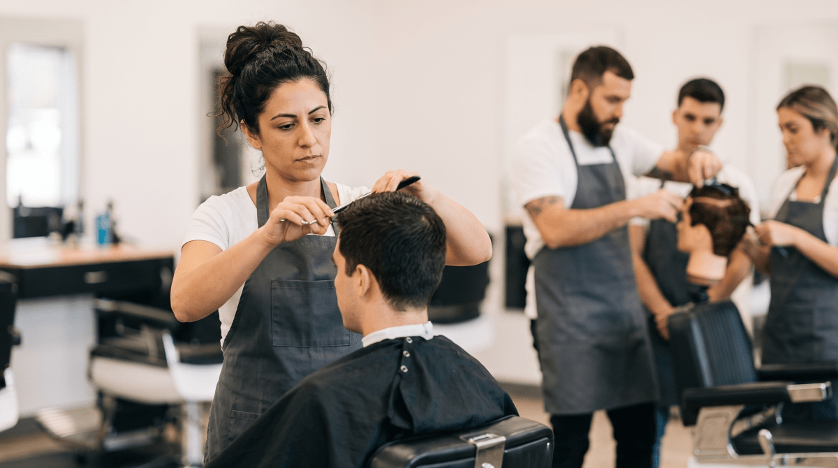 Barbering academy instructor teaching students at styling stations