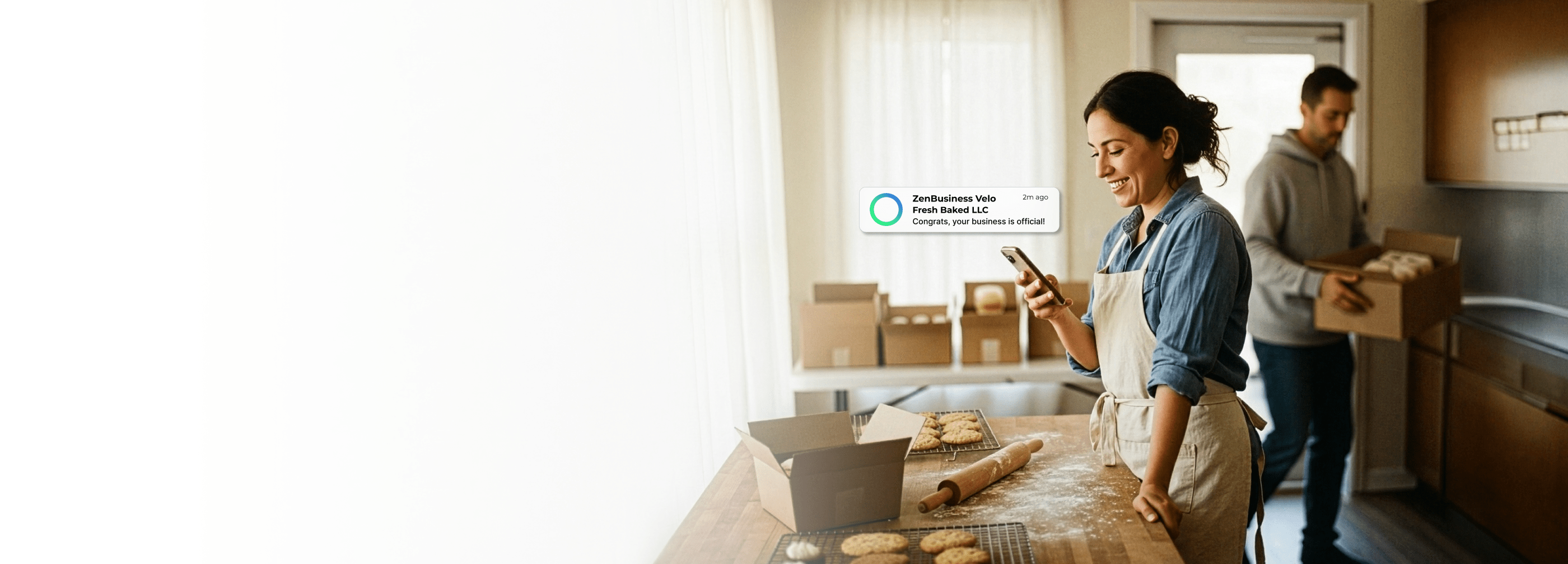 Professional small business owner using LLC formation service on phone at bakery with boxes and in a kitchen