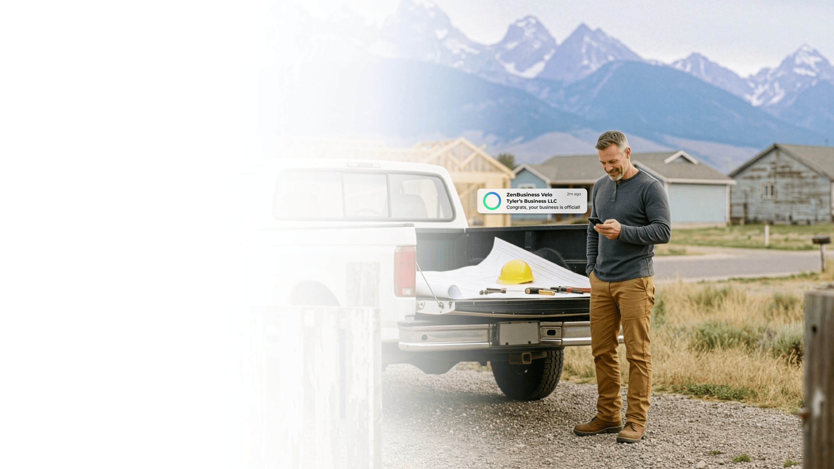 Male contractor in Wyoming checking his ZenBusiness Velo notification that his LLC is official while standing beside his pickup truck with blueprints and a hard hat in the truck bed and mountains in the background