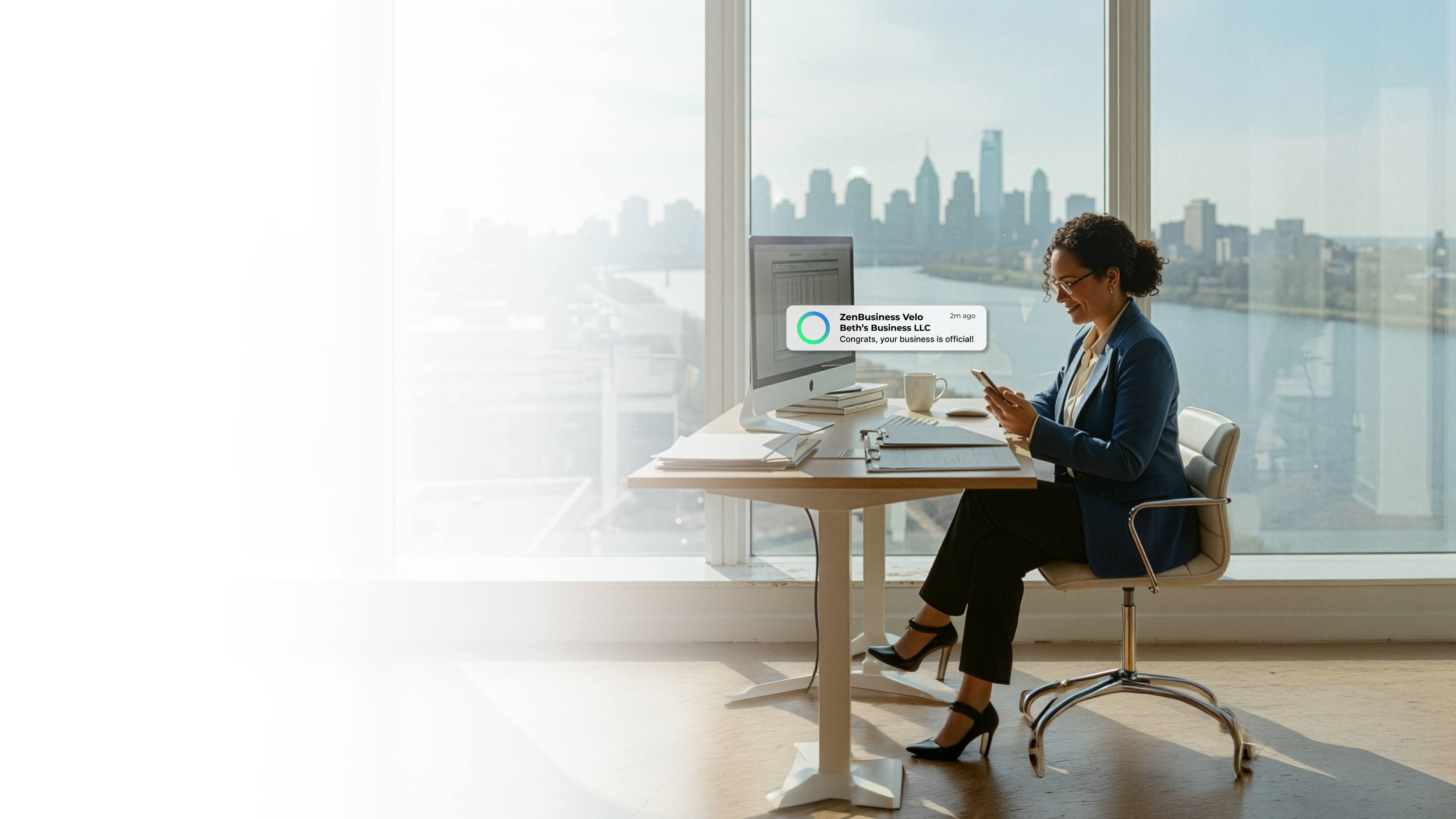 Female business professional at her desk in a Wilmington Delaware high-rise office with a river city skyline view after ZenBusiness Velo approved her LLC