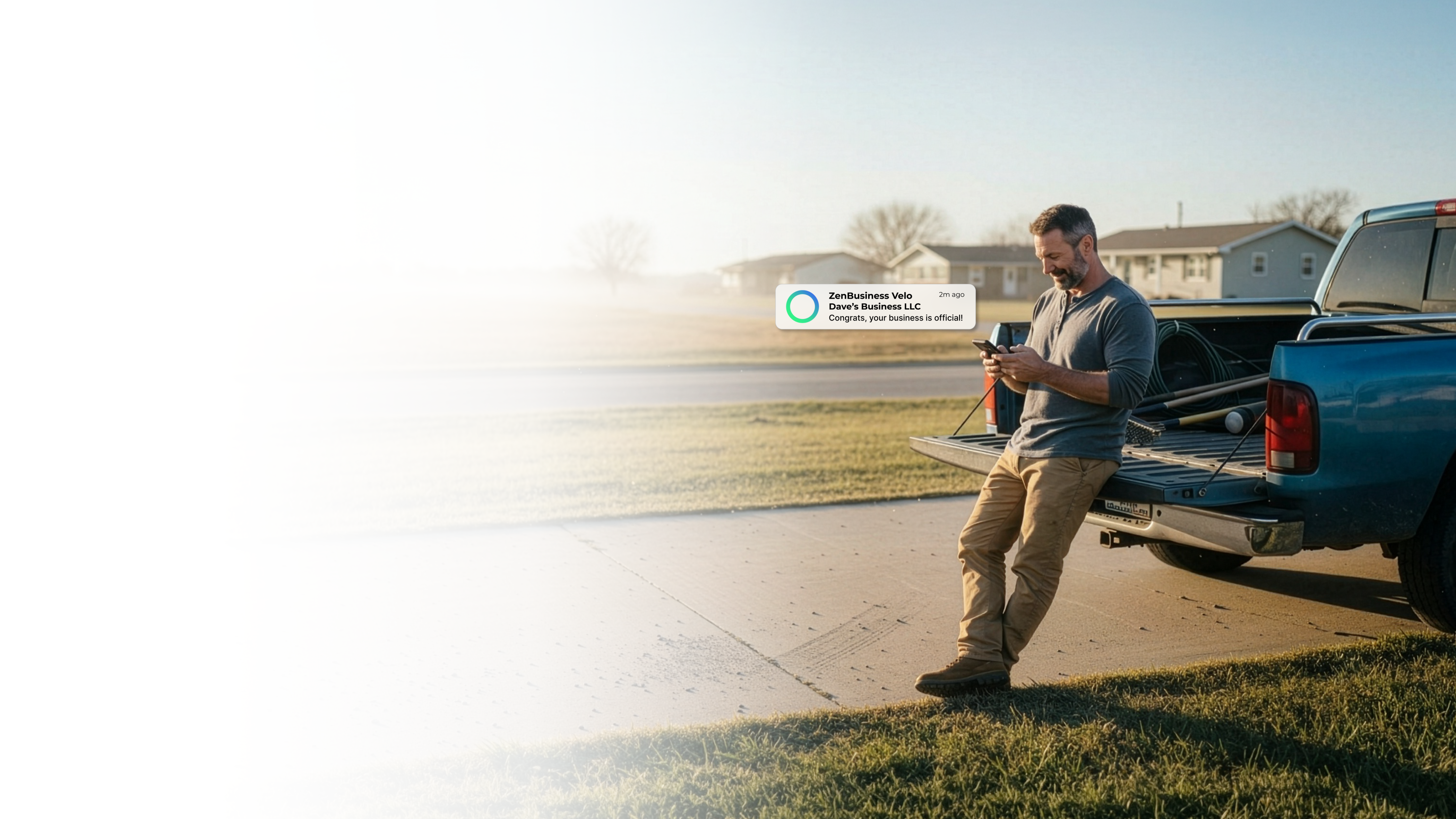 Male tradesman leaning against his work truck on a rural Kansas road at sunrise reading his ZenBusiness Velo notification that his LLC is official