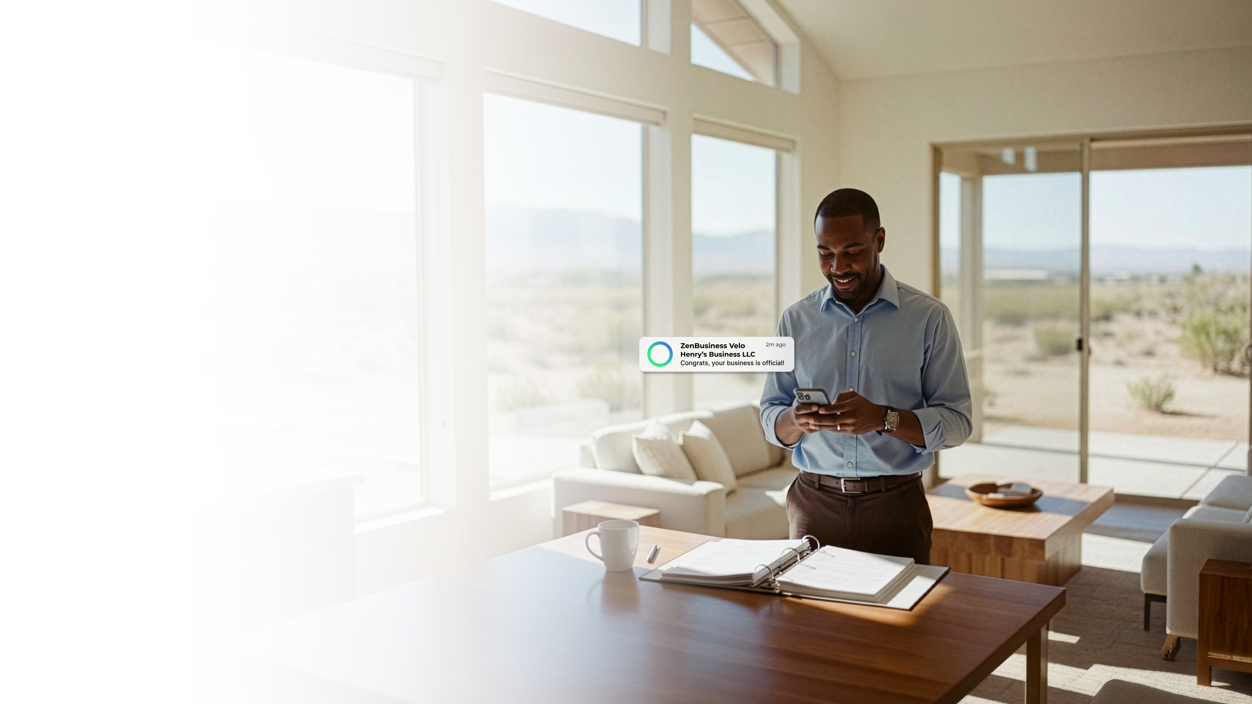 Male business owner in a modern Las Vegas Nevada home checking his ZenBusiness Velo notification confirming his LLC while standing in a bright open living space with desert views through floor-to-ceiling windows