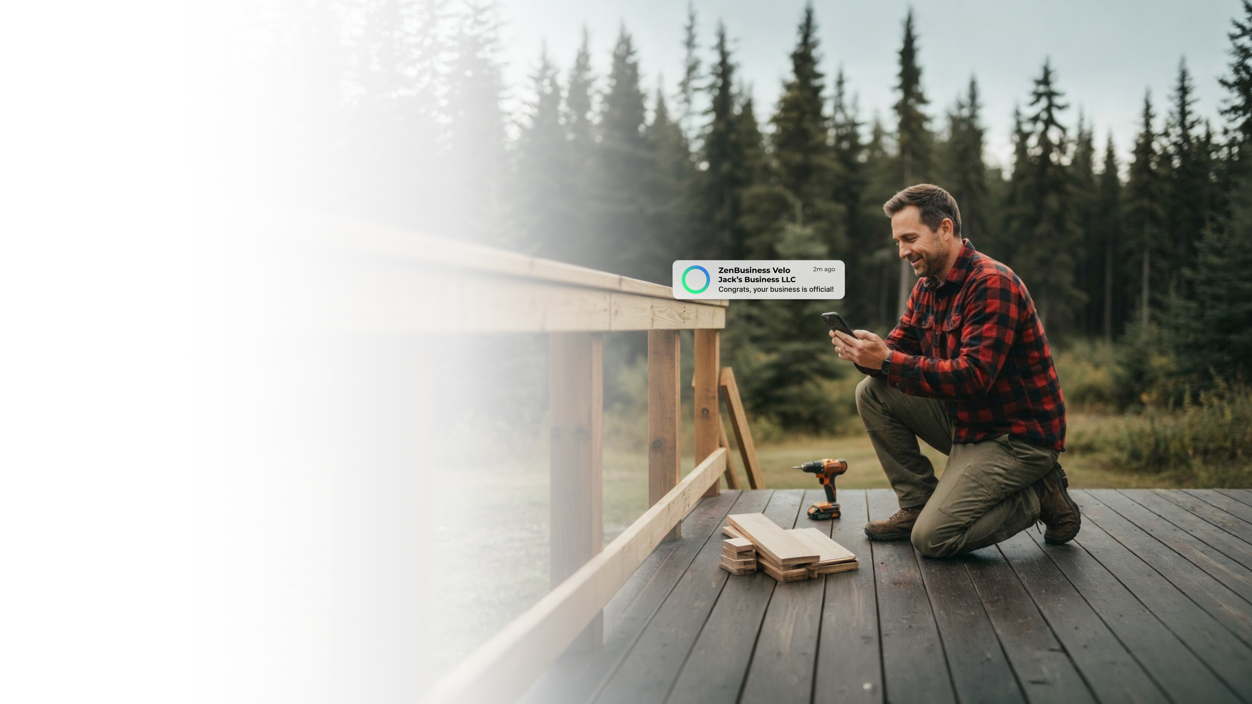 Male contractor kneeling on a deck he is building in an Alaska evergreen forest after ZenBusiness Velo confirmed his LLC is official
