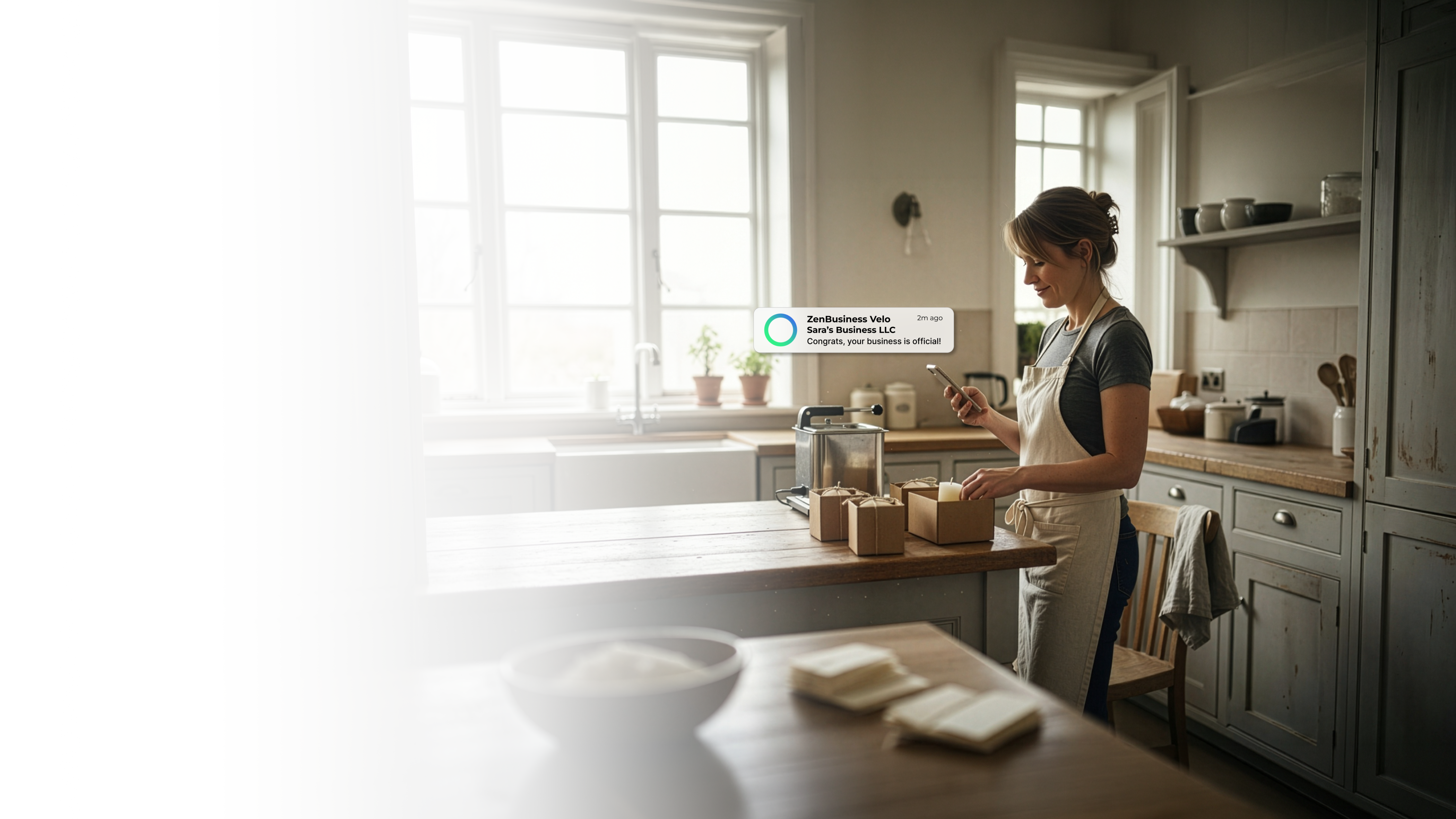 Female artisan soap maker in her Alabama home kitchen with handmade goods on the counter checking her ZenBusiness Velo notification that her LLC is approved