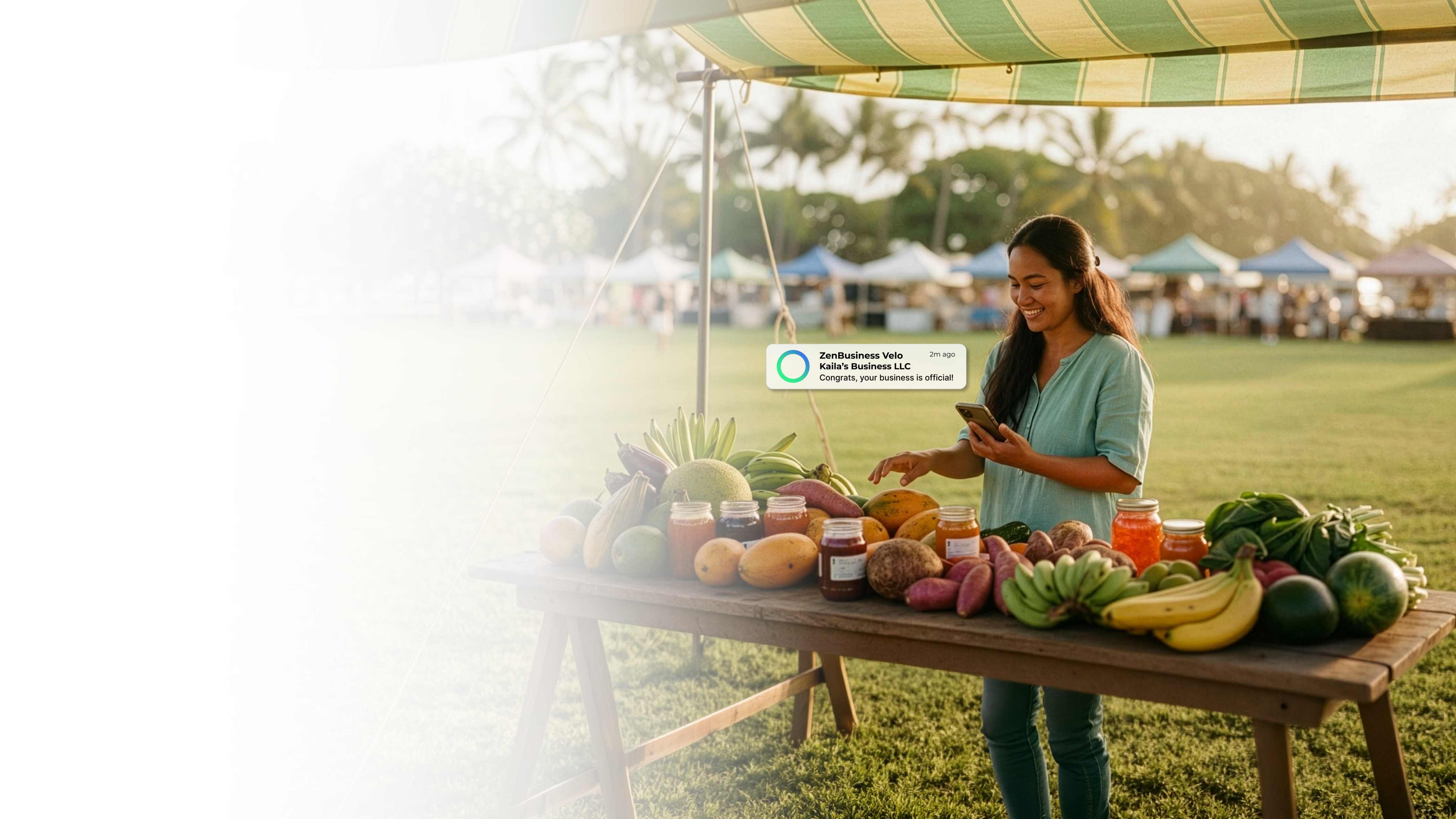 Female vendor at a Hawaii outdoor farmers market with tropical fruits on the table checking her ZenBusiness Velo notification that her LLC is official