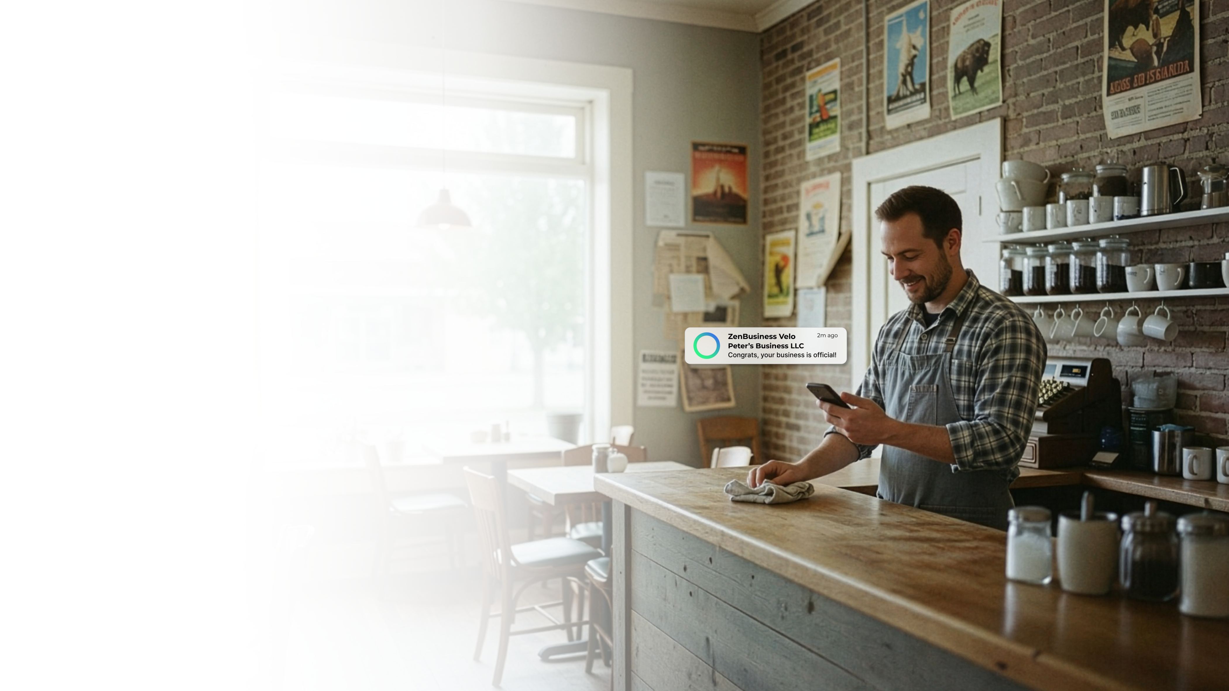 Male coffee shop owner in Fargo North Dakota reading his ZenBusiness Velo notification that his LLC is approved while behind the counter of his cozy cafe with an espresso machine nearby