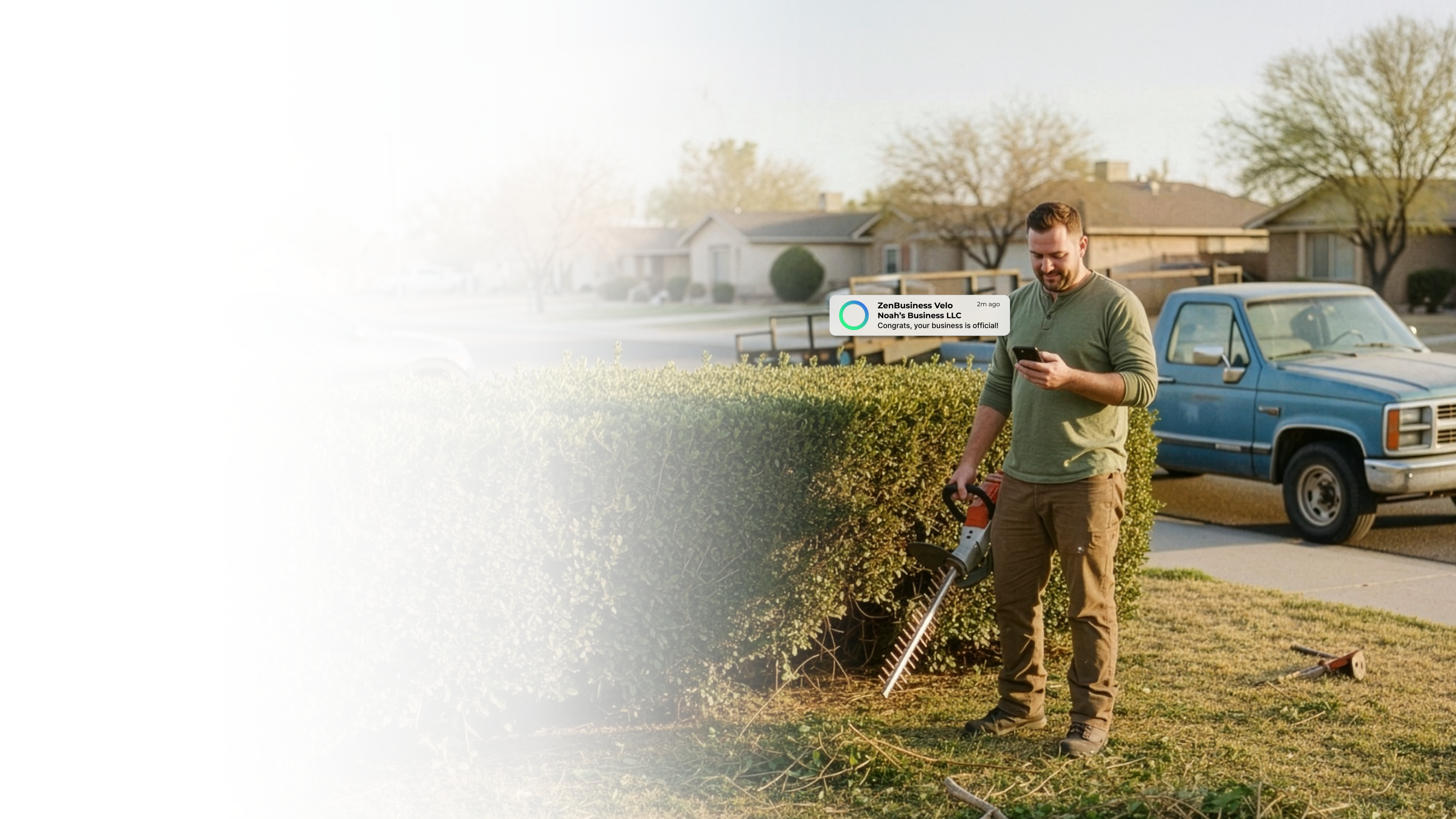 Male landscaper in Omaha Nebraska checking his ZenBusiness Velo notification that his LLC is official while trimming hedges outside a residential home with his work truck parked nearby