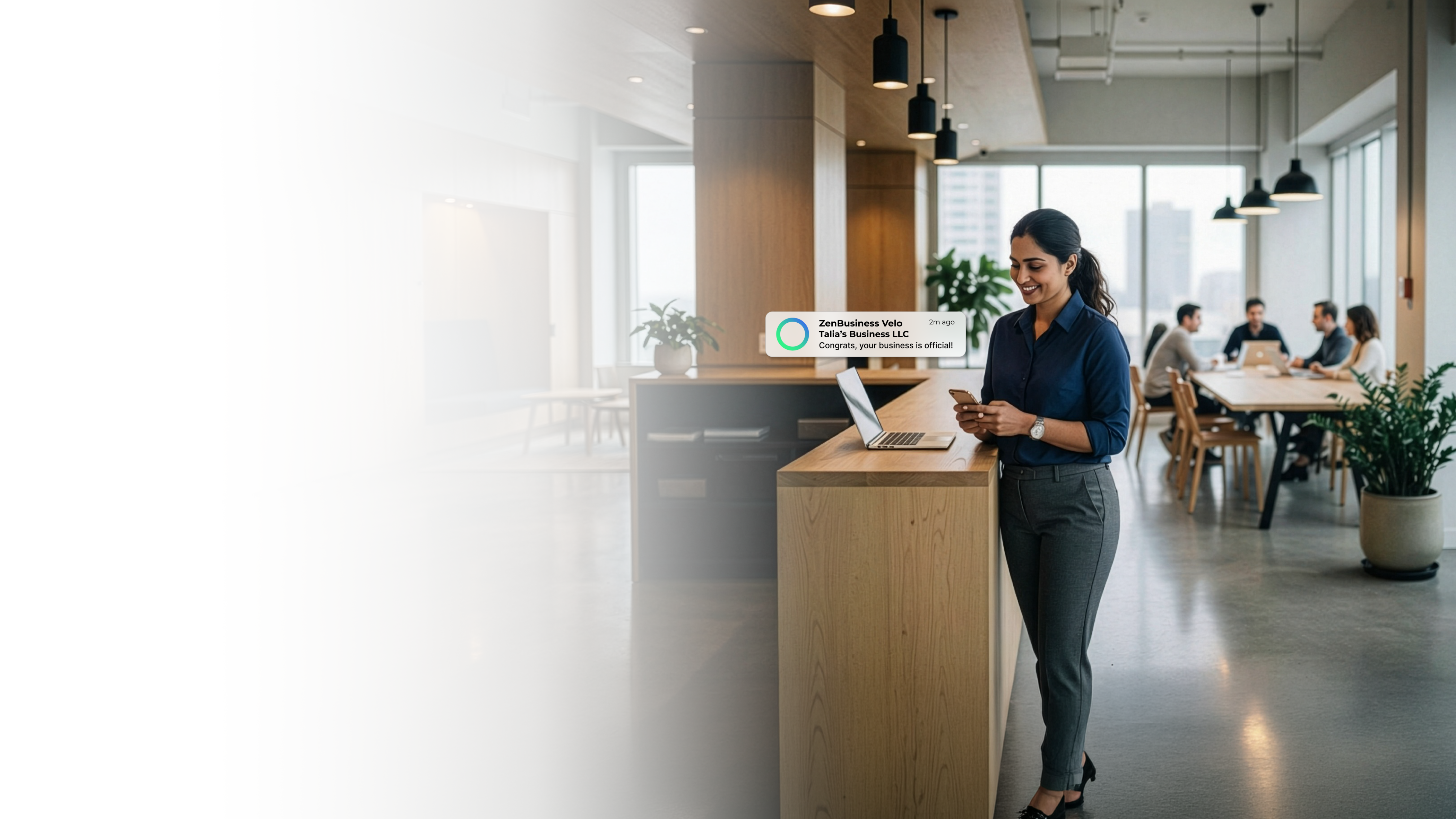 Female business owner at a standing desk in a modern New Jersey co-working space with a team meeting in the background after ZenBusiness Velo approved her LLC