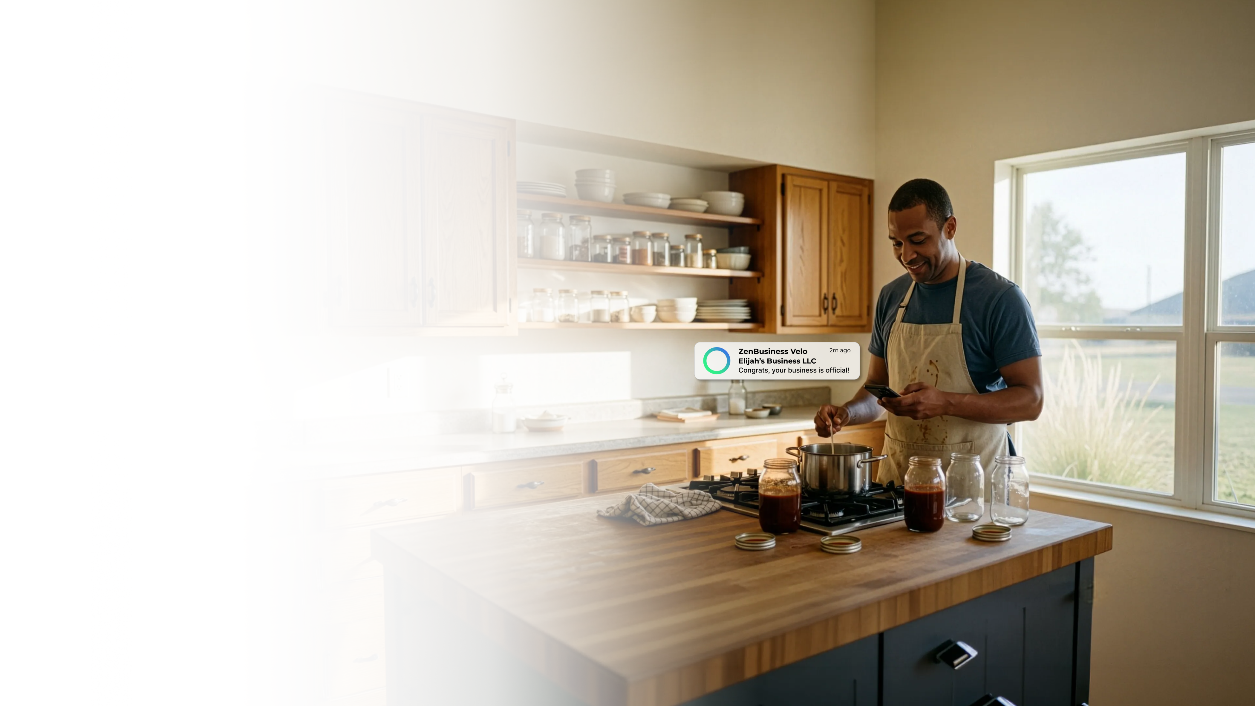 Male food entrepreneur in an Oklahoma home kitchen checking his ZenBusiness Velo notification confirming his LLC while cooking with mason jars and spices on open wooden shelves behind him