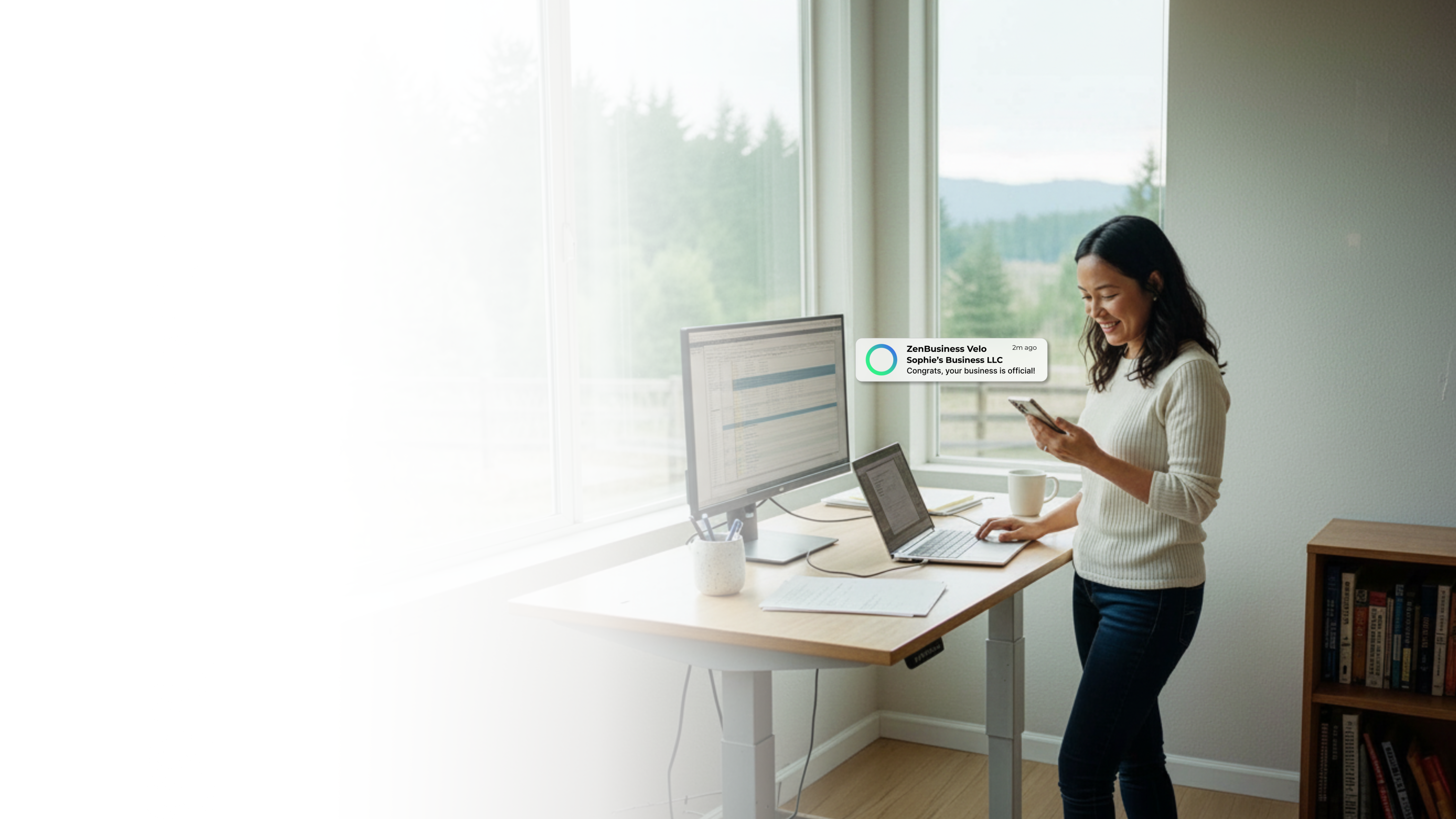 Female tech entrepreneur at a standing desk in a Portland Oregon home office checking her ZenBusiness Velo notification that her LLC is official with a rainy Pacific Northwest forest outside the window