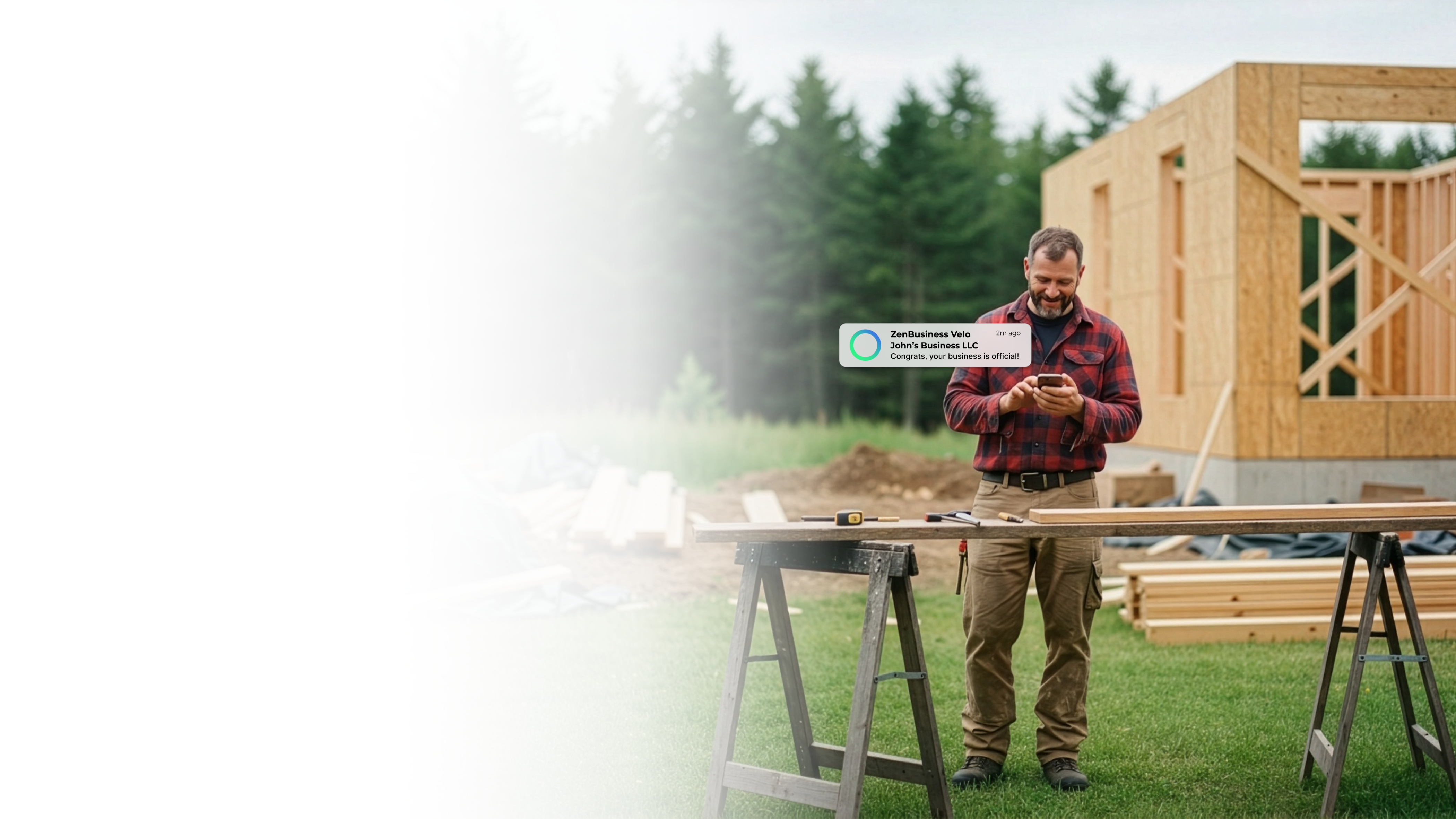 Male carpenter in Vermont checking his ZenBusiness Velo notification confirming his LLC while standing at a workbench outside a timber frame structure surrounded by green forest