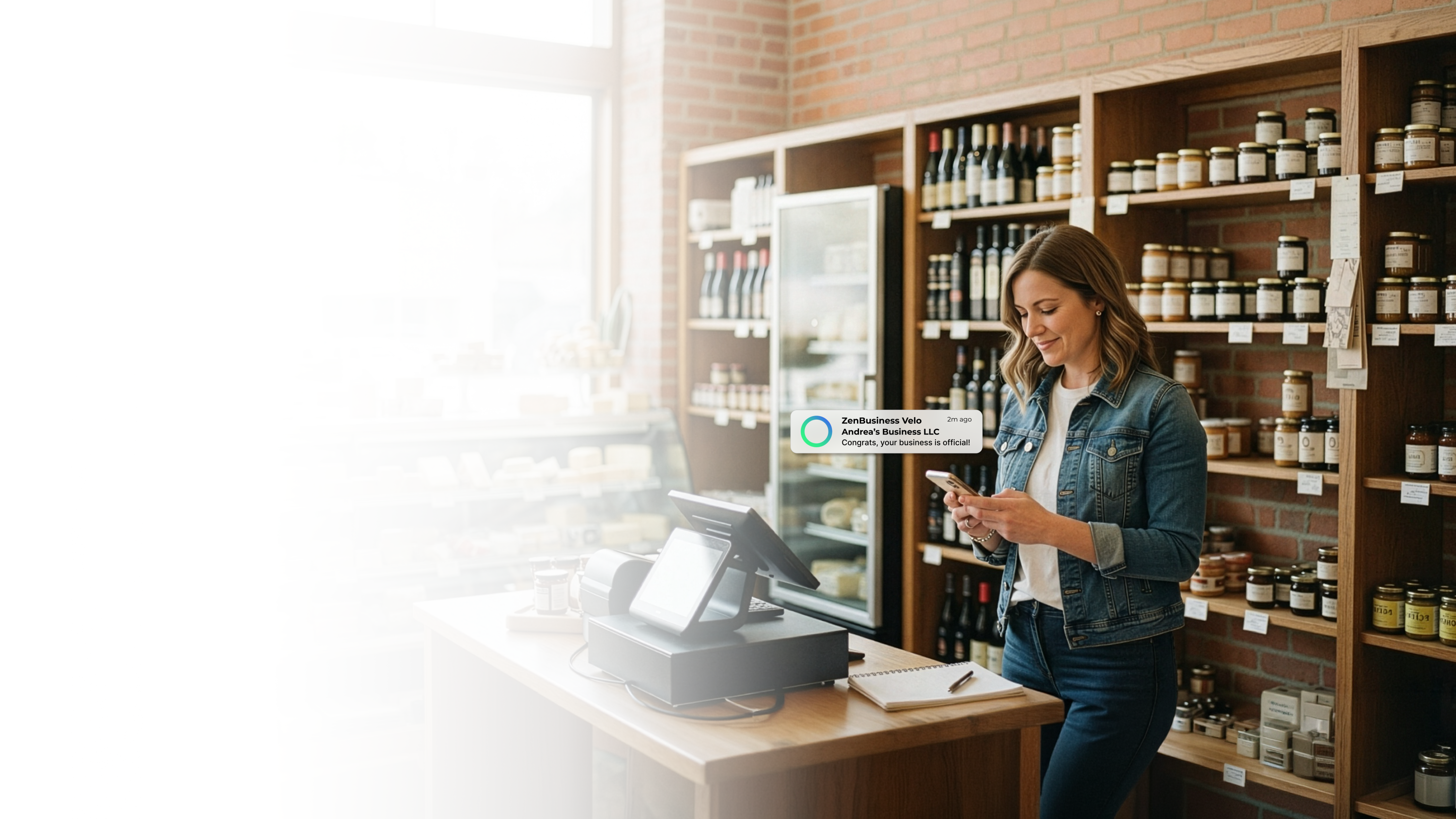 Female specialty food shop owner in Wisconsin reading her ZenBusiness Velo notification confirming her LLC while standing at the counter of her store stocked with jars, wine, and artisan goods