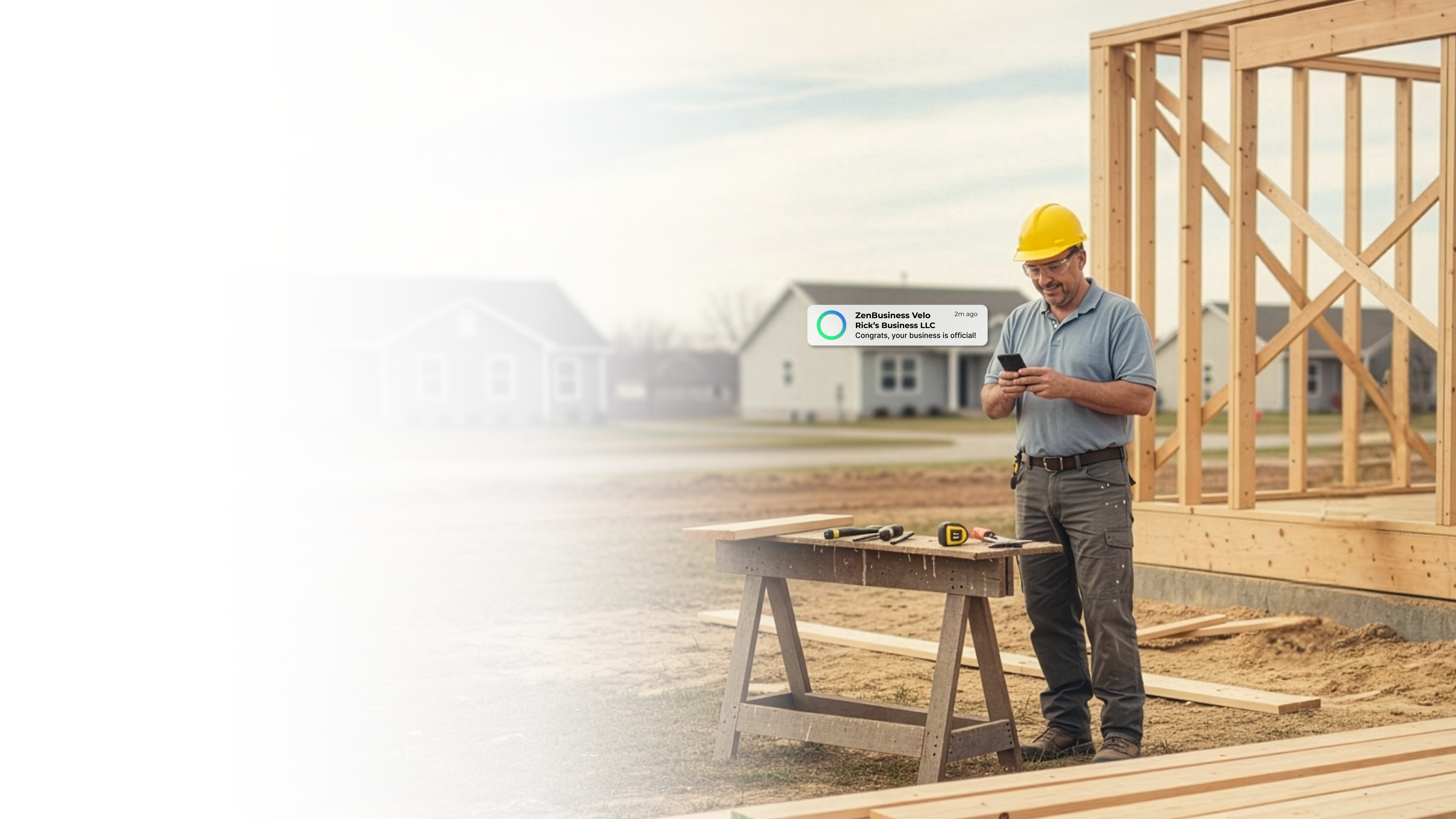 Male construction contractor in a hard hat on a Missouri job site checking his phone after ZenBusiness Velo confirmed his LLC is official with a newly framed structure behind him