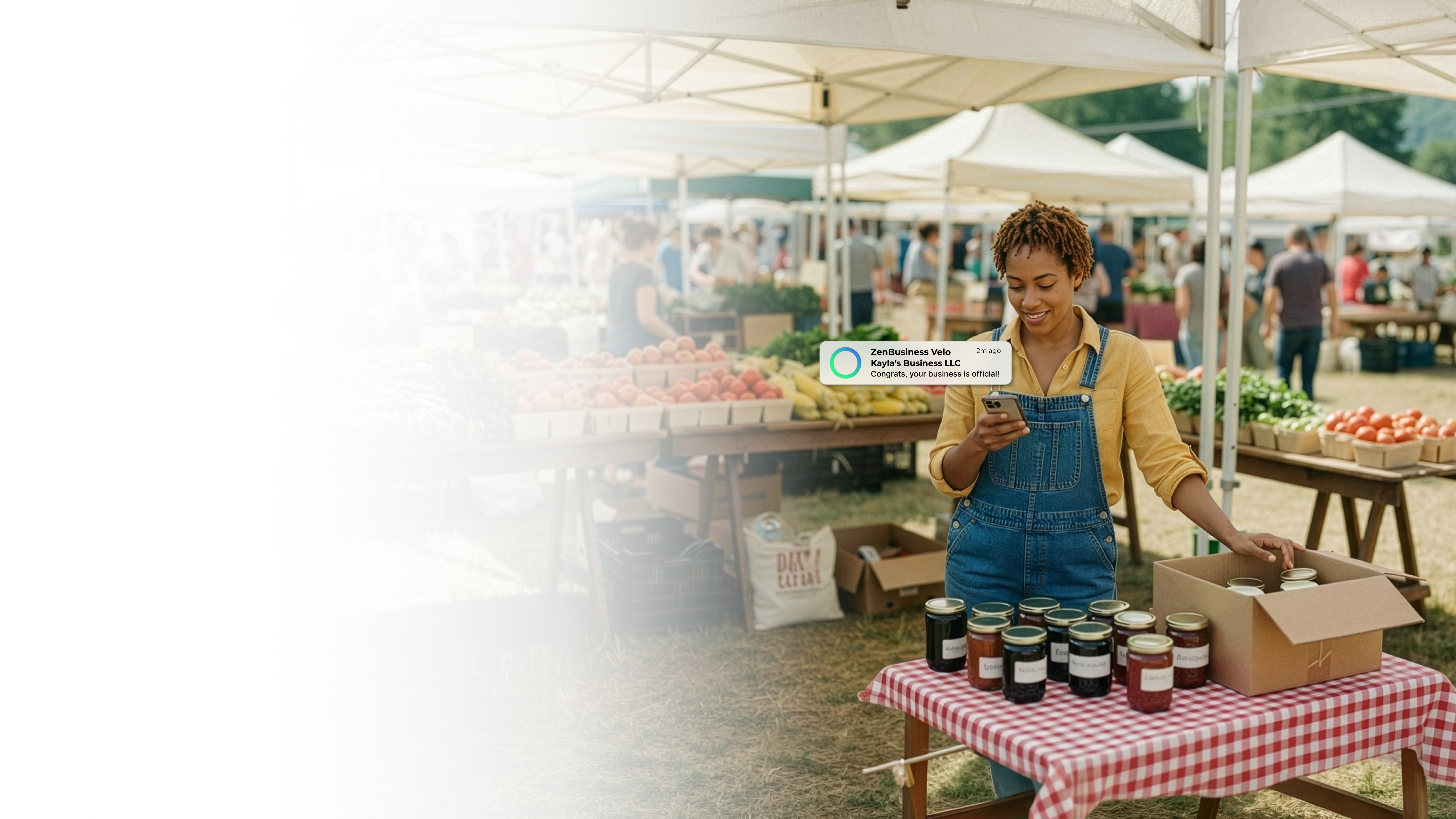 Female farmers market vendor in West Virginia smiling at her ZenBusiness Velo notification confirming her LLC while standing behind a table of jars and fresh produce at a busy outdoor market