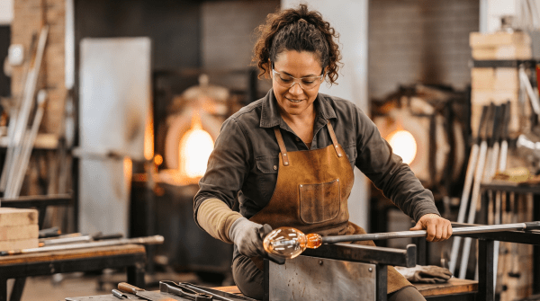 Glassblower shaping molten glass at the furnace in a studio