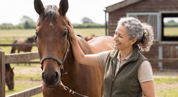 Horseback riding school owner leading a horse through an outdoor arena