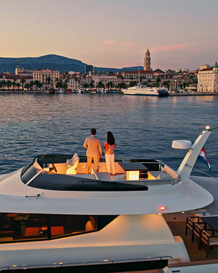 Couple stands on yacht admiring coastal town at sunset.