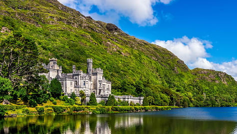 Beautiful castle like Kylemore Abbey reflected in lake at the foot of a mountain in Connemara, Ireland.