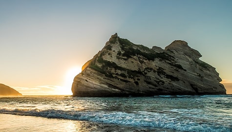 Sun rising behind the rock formation at Wharariki Beach on the South Island of New Zealand.